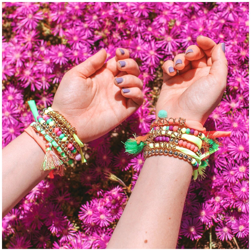 Neo-Brite chains and charms showcase two metallic finish bracelets with colorful tassels and pink fabric flowers in the backg