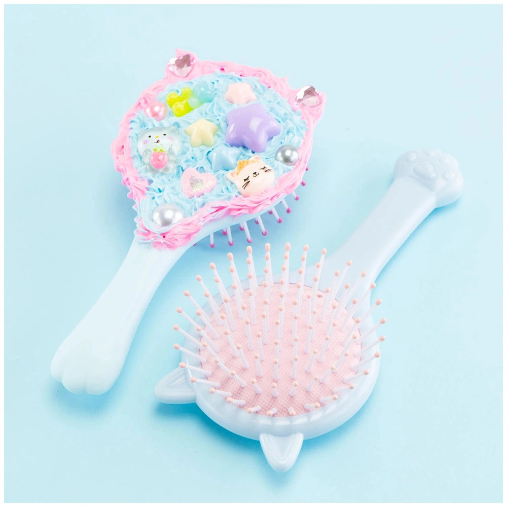 Momomi Decoden Kawaii Artist brush features a pink head with white bristles and a white handle on a blue surface.