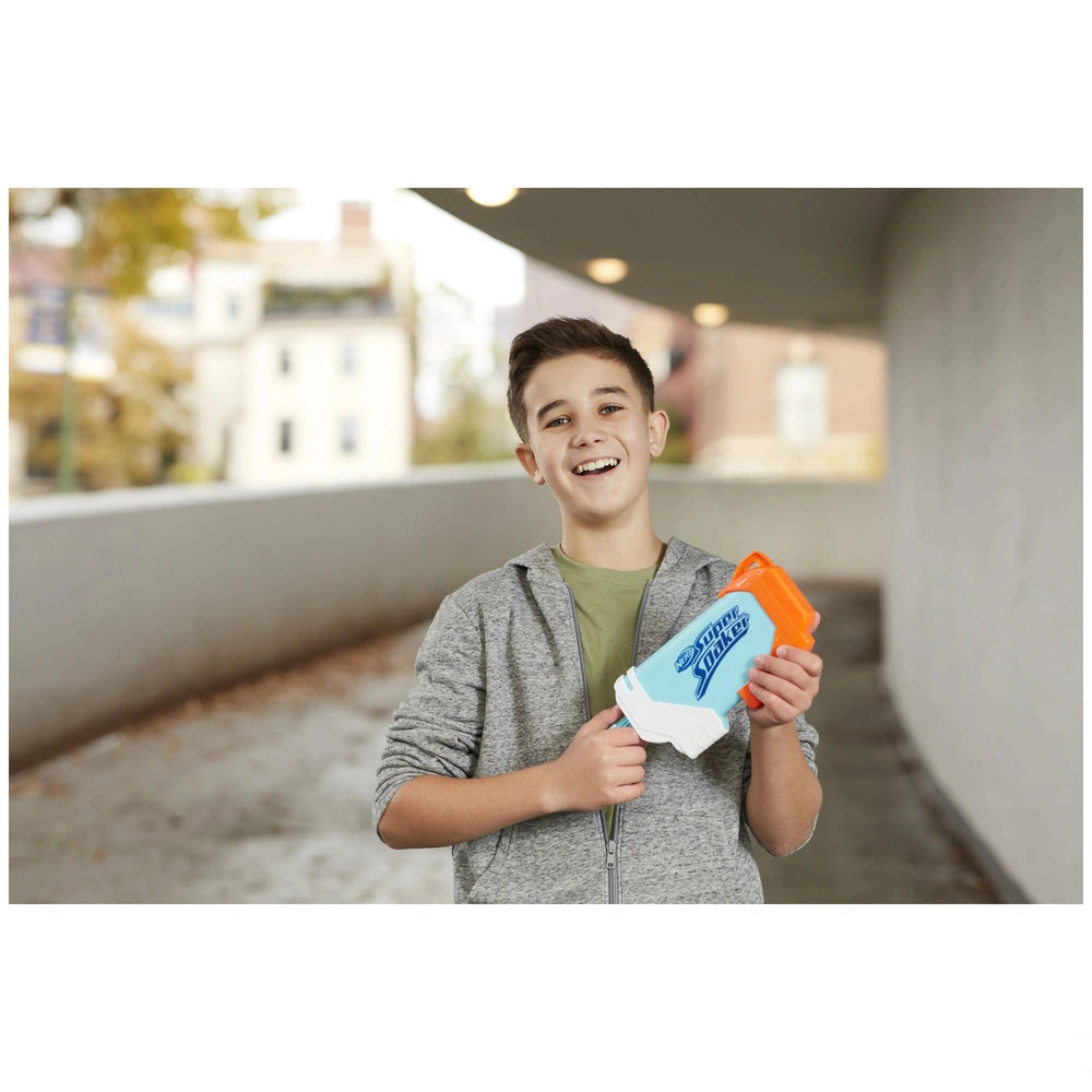 Nerf Super Soaker Torrent Water Blaster held by a boy in a gray hoodie, standing on gray concrete with trees and a building b