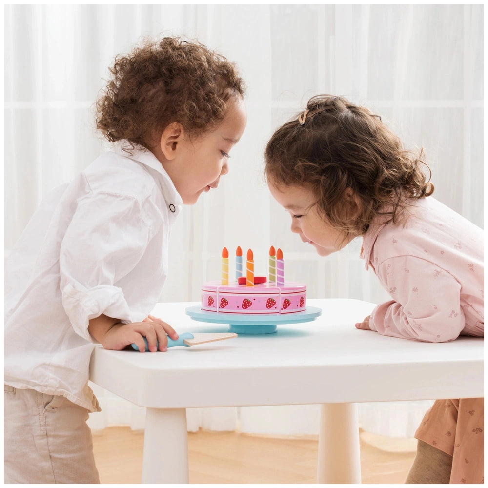 New Classic Toys Cutting Cake set with pink cake, blue candle holder, and two children celebrating at a white table.