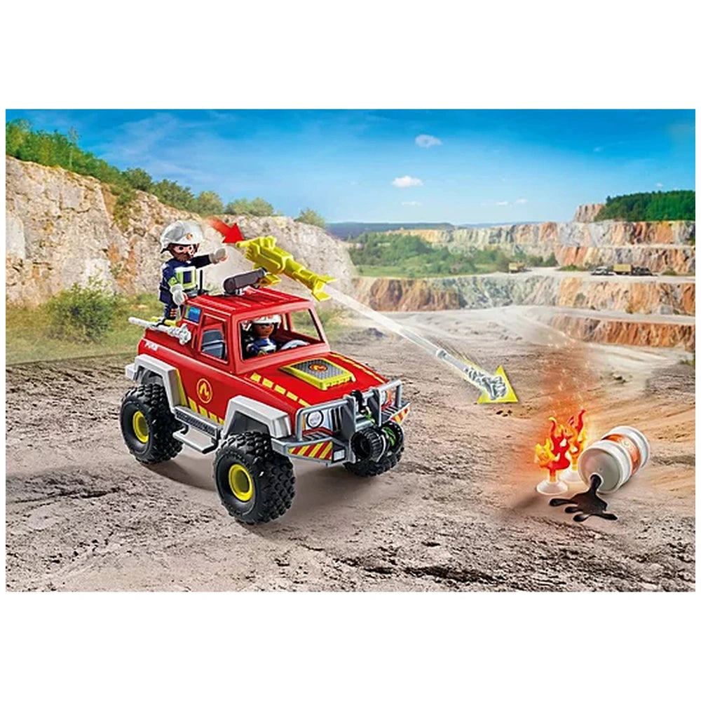 red PLAYMOBIL firefighting truck with two helmeted figures atop, against a rocky cliff and clear sky backdrop.