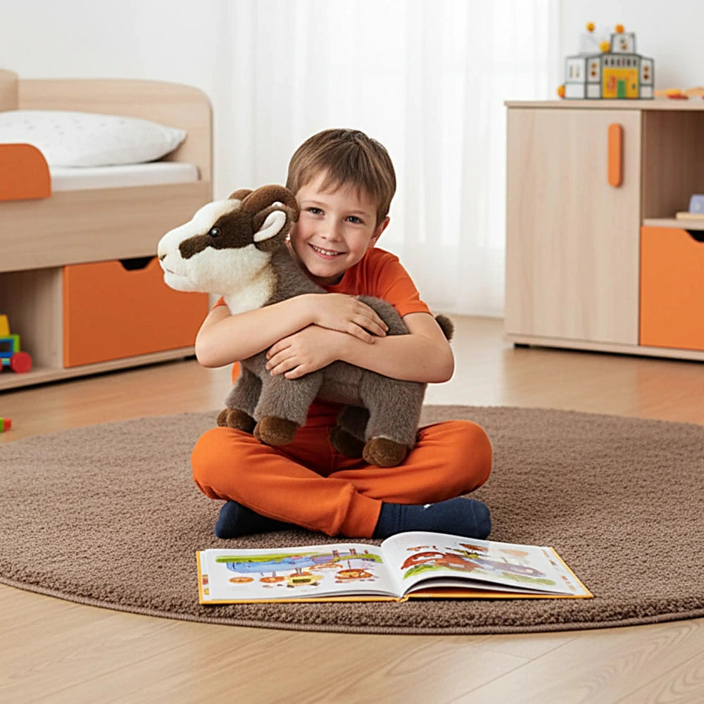 Rudy Little Mountain Chamois plush held by a young boy sitting on a brown carpet with a book nearby in a bright room.