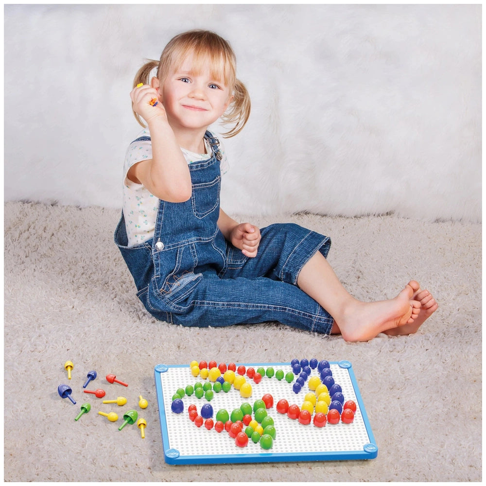 Young girl in denim jumpsuit smiles while playing with colorful Quercetti FantaColor Tab objects on a fluffy white rug.