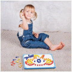 Young girl in denim jumpsuit playing with Quercetti FantaColor Tab toy on light carpet, smiling as she arranges colorful bead