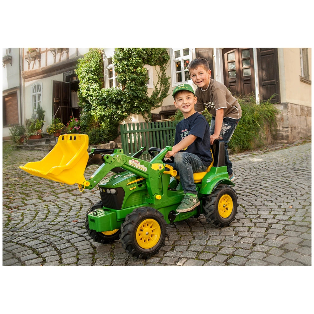 Green and yellow Rollyfarmtrac John Deere 7930 four-wheeler with two boys in casual clothing on a cobblestone street.