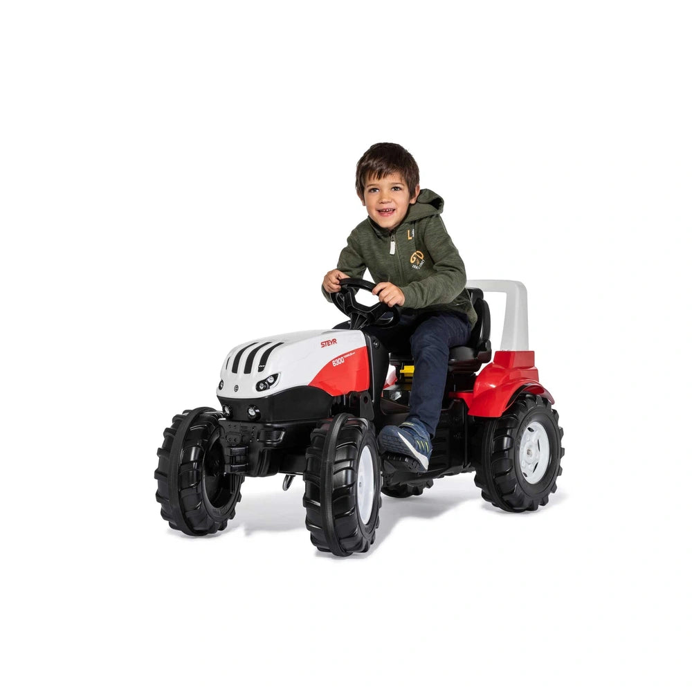 Rollyfarmtrac Premium II Steyr 6300 Terrus CVT toy tractor with a smiling child in a green jacket sitting and steering.