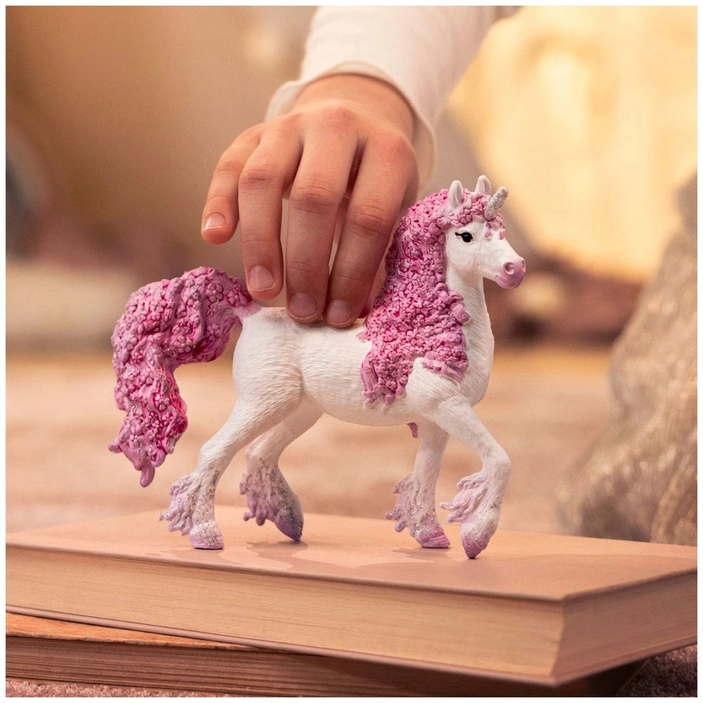 A hand holds a glossy white and pink unicorn figurine with detailed features in a warm indoor setting.