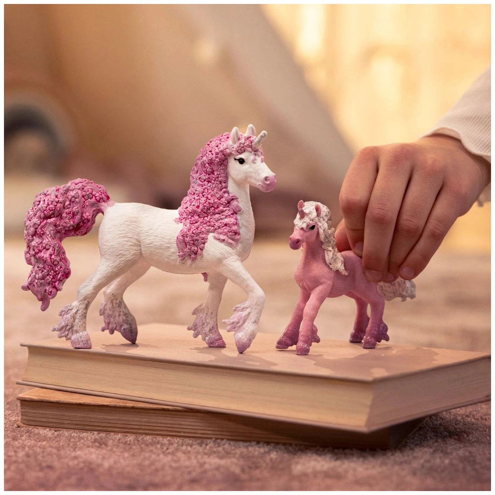 Pink and white unicorn figurine with a pink mane and tail, held above a smooth, light-colored hardcover book.