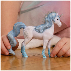 Flowy unicorn mare figurine with a glossy white body and blue highlights, held gently by a hand on a wooden surface.