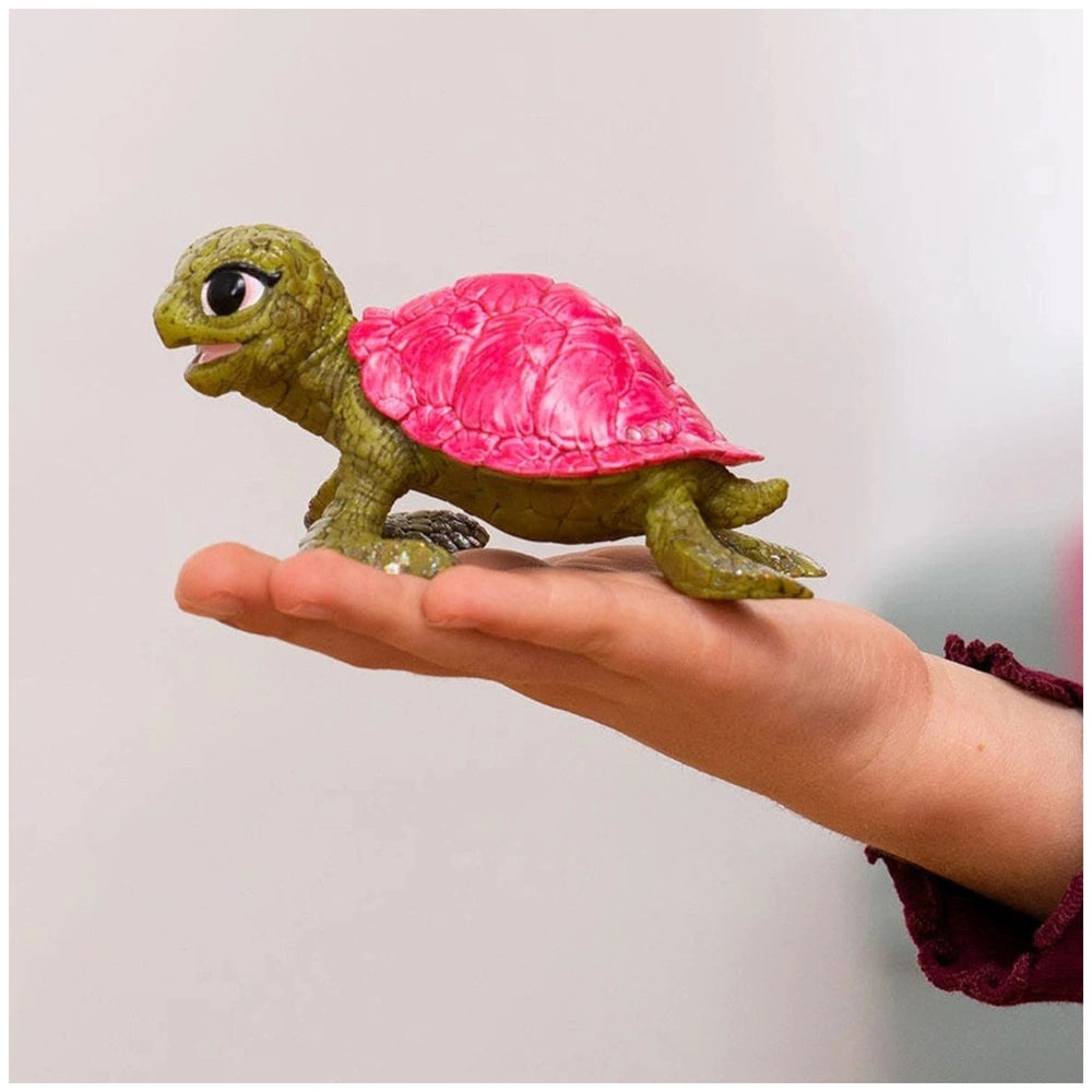 Green toy turtle with a pink shell held in a hand against a plain light background.