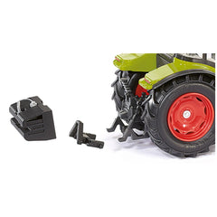 Green and red toy tractor with large black tires, positioned next to a black plastic part on a light-colored surface.