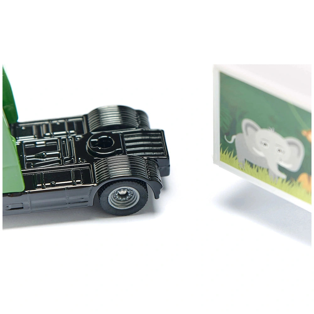 Articulated truck with trailer in black metallic finish alongside a cardboard elephant cutout on green grass.