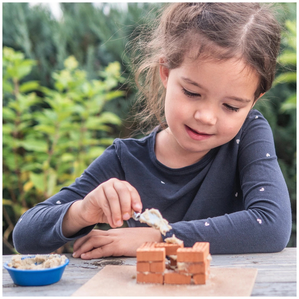 Teifoc small family home set features a young girl in a blue shirt engaged with a brown brick structure at a wooden table.