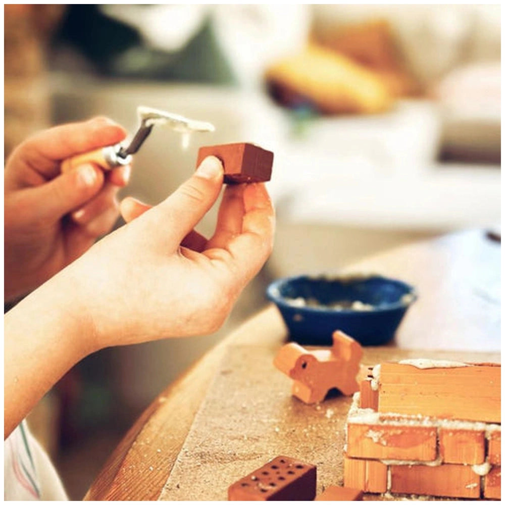 Teifoc trowel tool is used by hands shaping a small clay object on a wooden surface in a crafting activity.