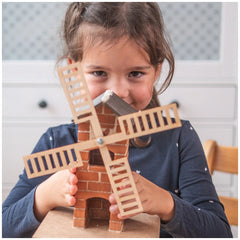 Teifoc windmill craft with brown and beige wooden blocks and blades, as a girl in a blue shirt plays in the foreground.