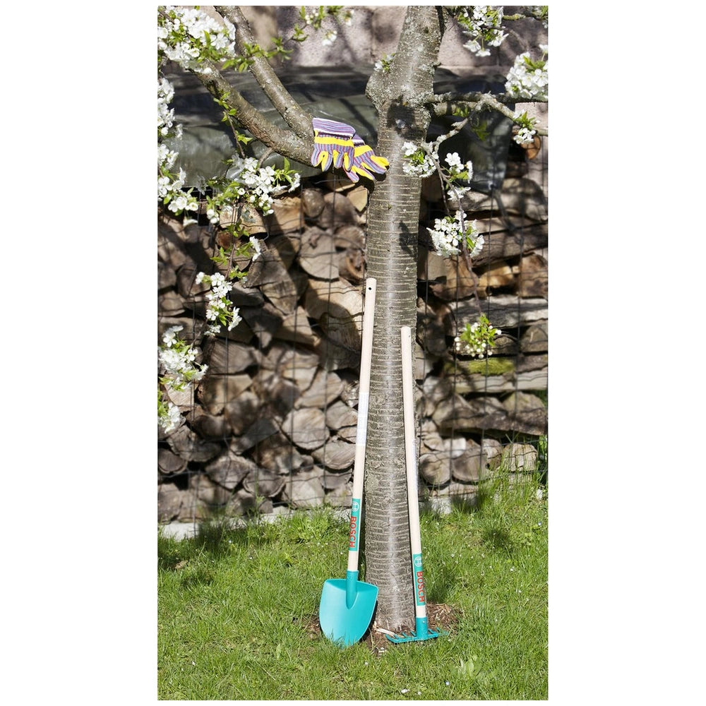 Theo Klein Bosch Garden Gardener Set with blue shovel and yellow-purple tool on grass near flowering tree and wooden fence.