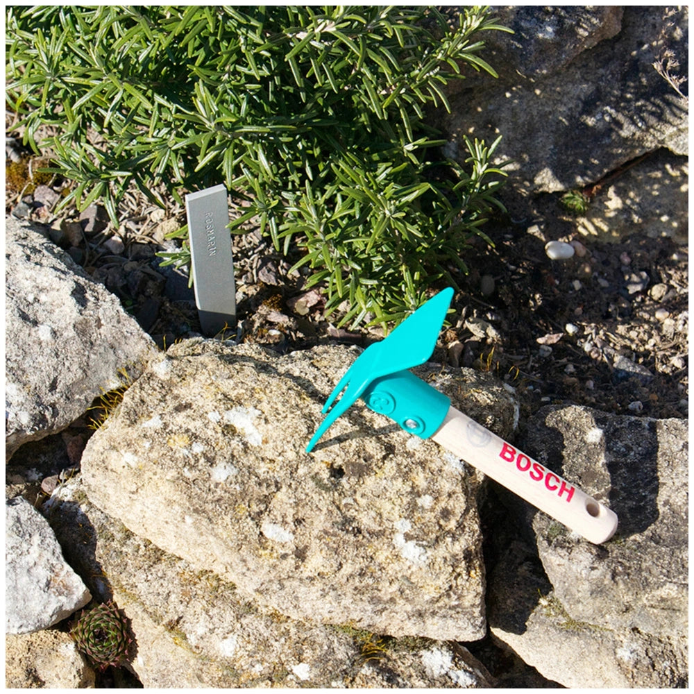 Theo Klein Bosch garden hoe with white handle, green blade, blue grip, and silver bolt, set against a gray rock background.