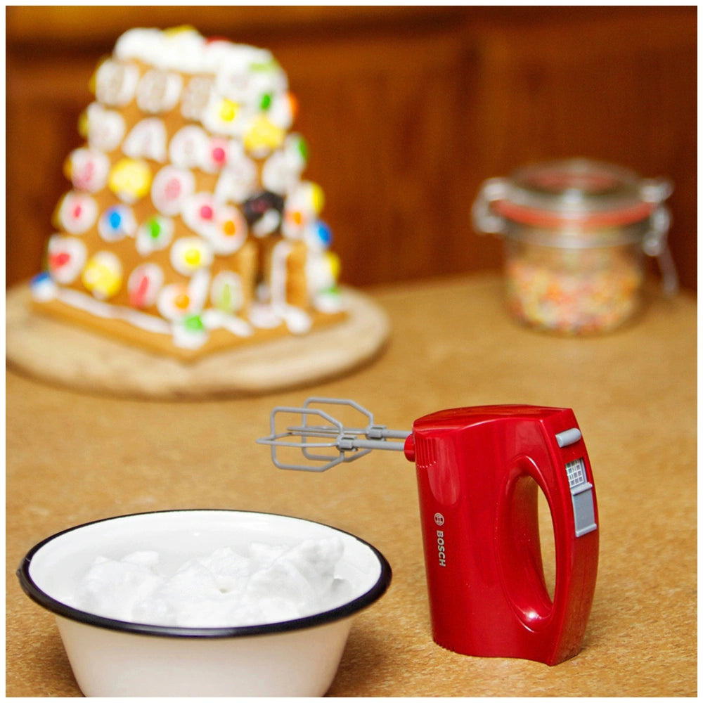 Theo Klein Bosch handmixer with a white ceramic bowl and red plastic whisk, displayed centrally on a table.
