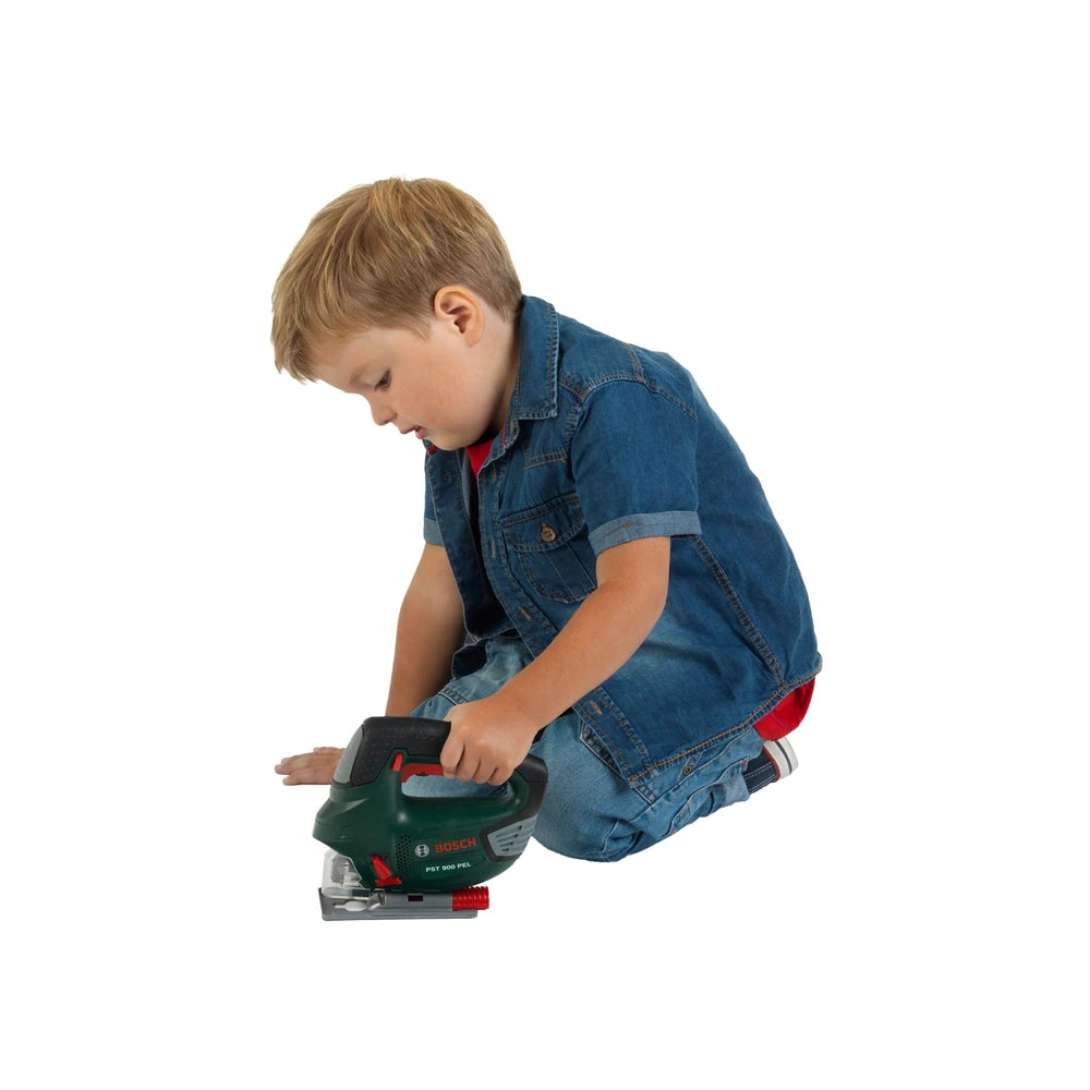 Young child with blonde hair in a blue denim jacket and red t-shirt holds a green and black pretend Bosch jigsaw on a white s