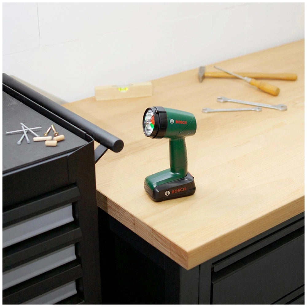 Theo Klein Bosch lamp on a brown wooden table with green and black power tool and silver metal tools nearby.